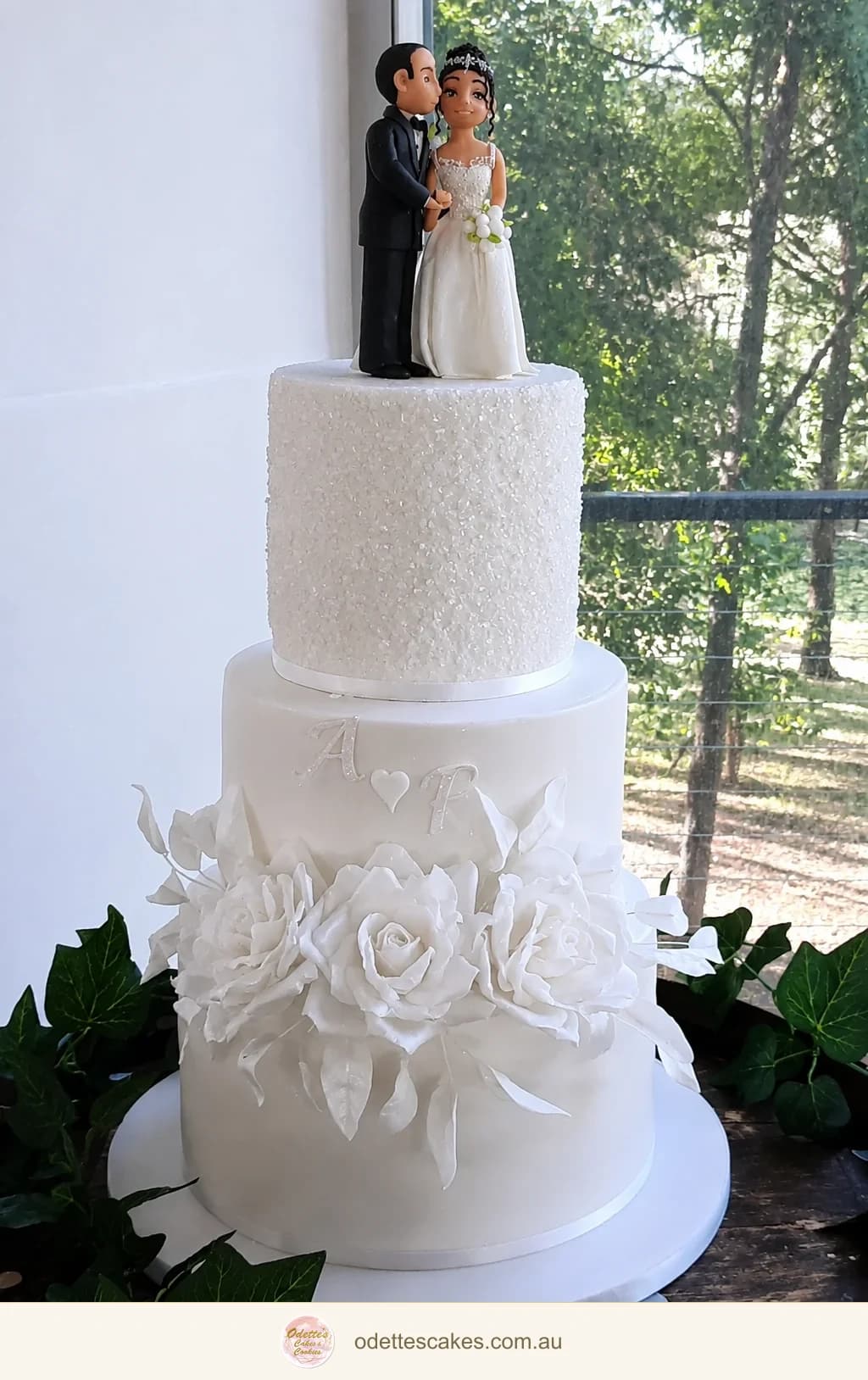 Three-tier white wedding cake with white floral decoration and a couple figurine topper