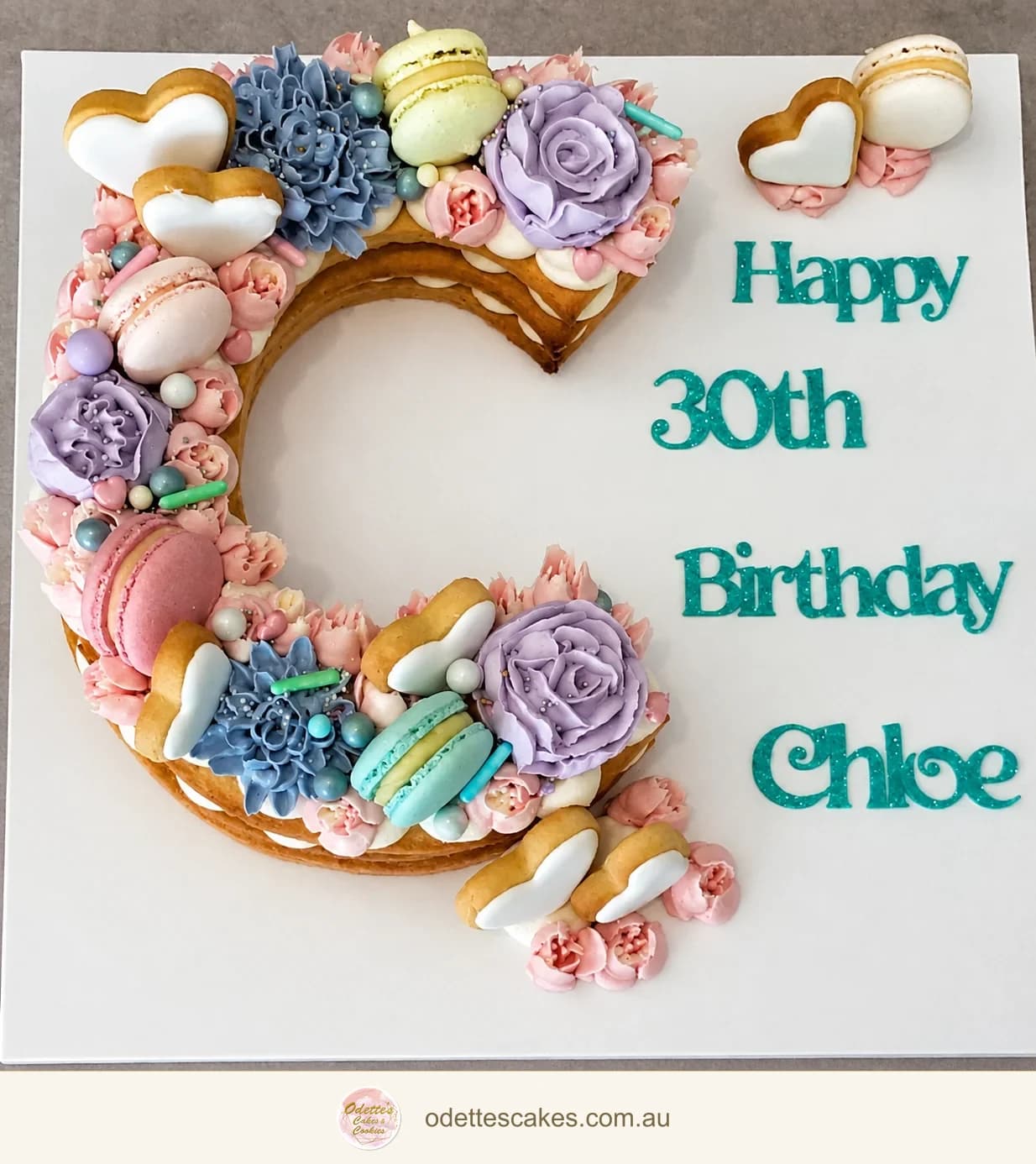 Letter C cookie cake decorated with pastel flowers, macarons and piped cream for a 30th birthday