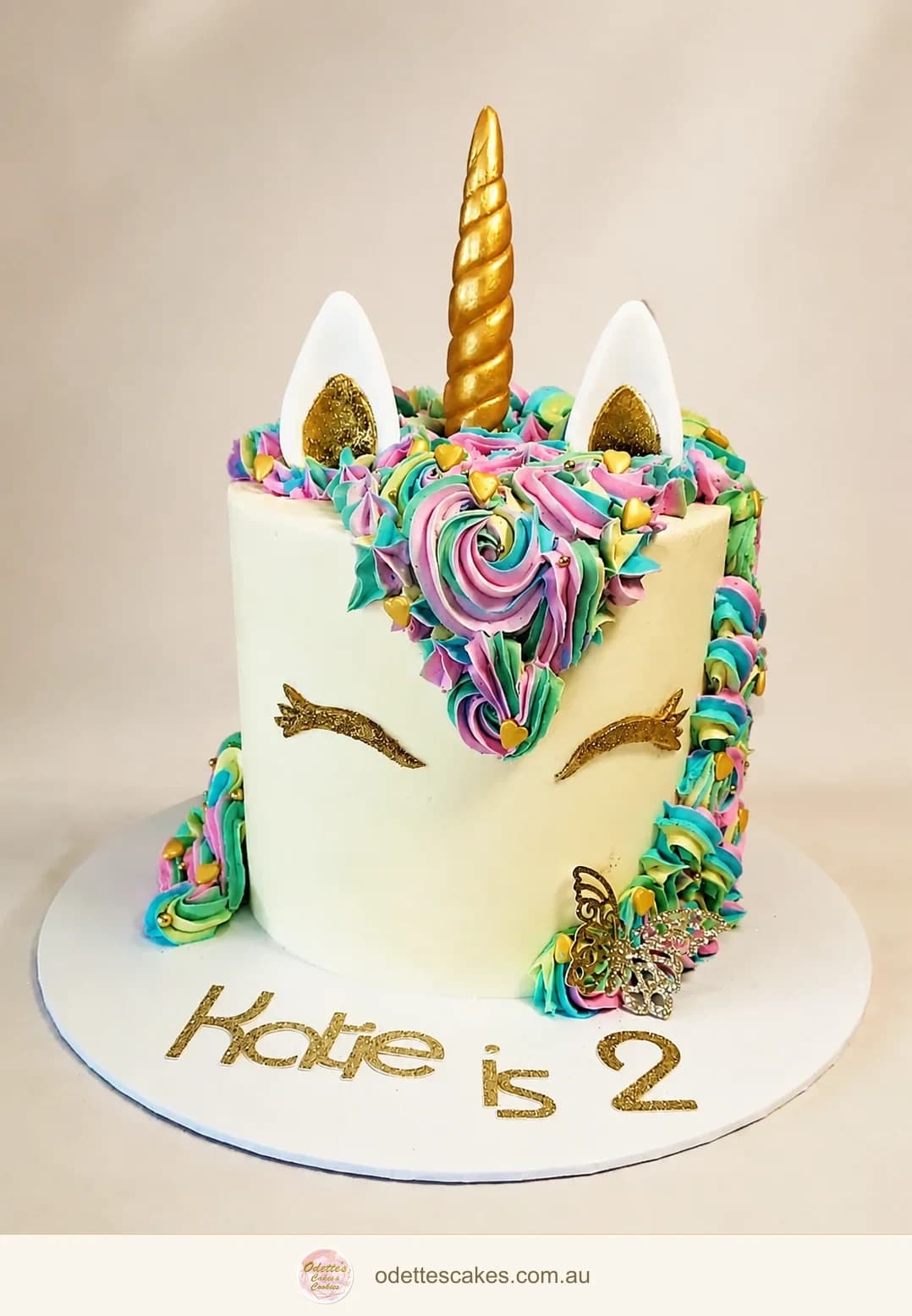 Pastel unicorn birthday cake with a gold horn, piped rainbow mane and butterfly details
