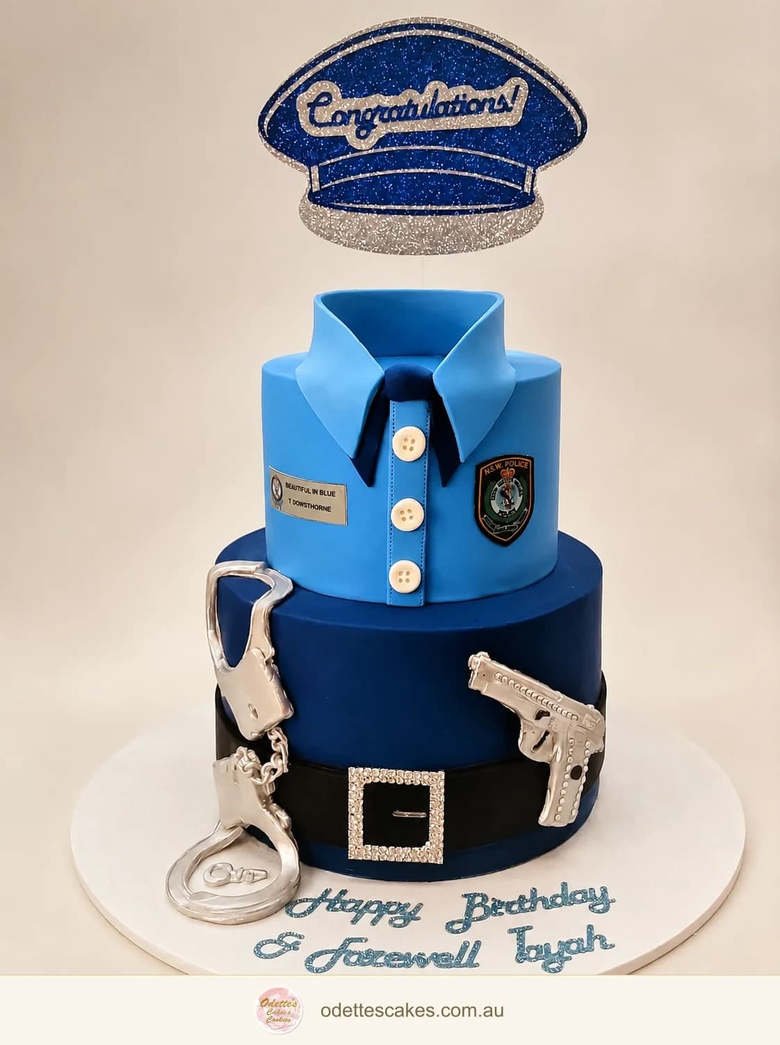 Two-tier police-themed blue birthday cake with a uniform shirt, cap and handcuff details