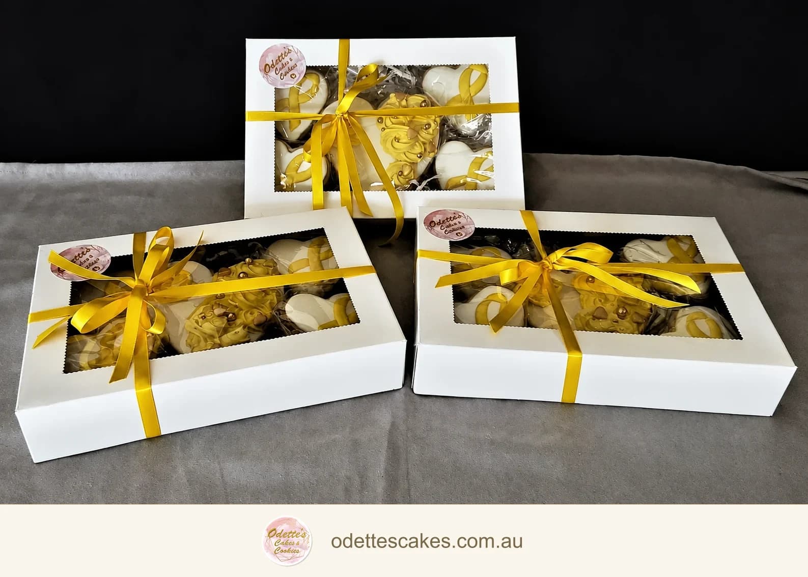 Gift boxes of pale yellow and white decorated cookies tied with gold ribbon