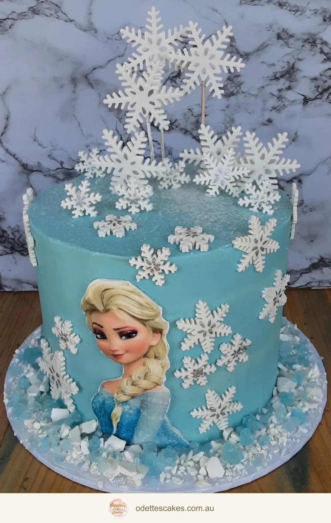 Blue Frozen-themed birthday cake with Elsa decoration and delicate white snowflakes