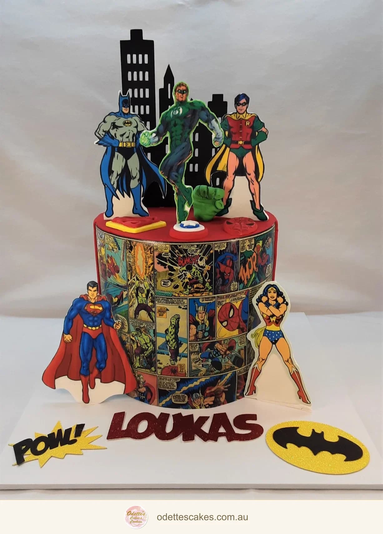 Two-tier superhero birthday cake with comic-book characters, a city skyline and a personalised base
