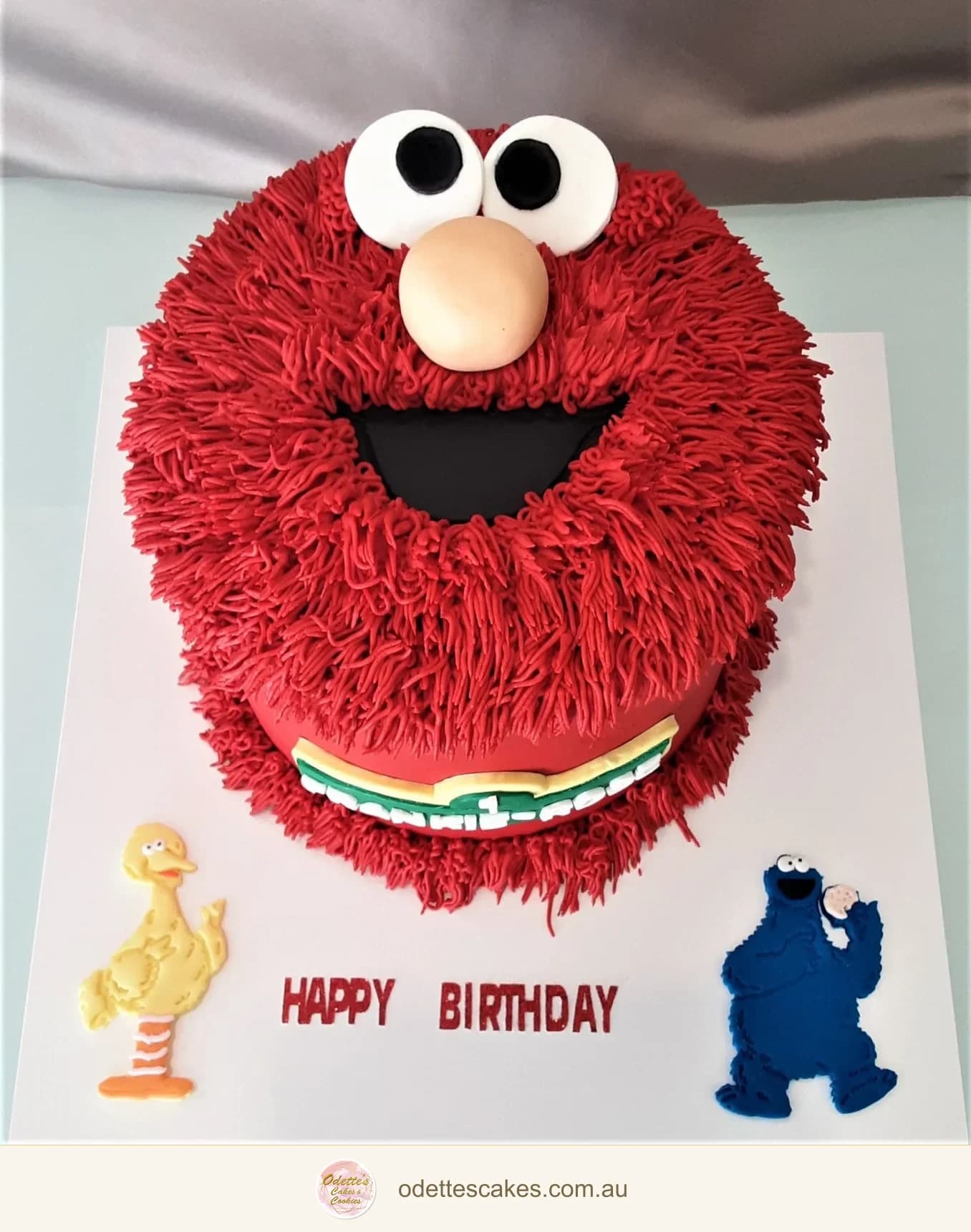 Round red Elmo birthday cake with piped fur, large white eyes and an orange nose
