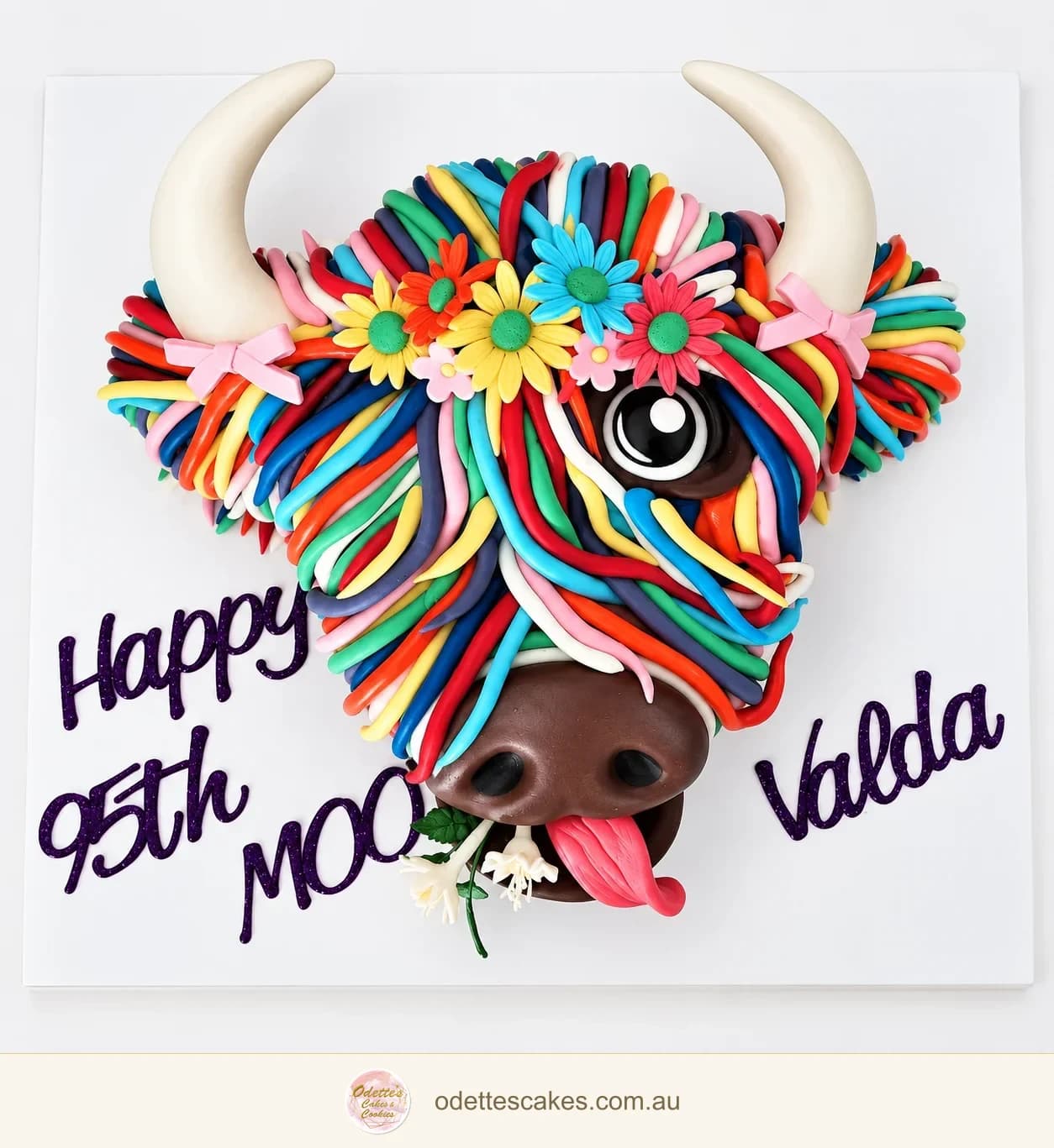 Sculpted Highland cow birthday cake with a colourful rainbow mane, flowers and white horns
