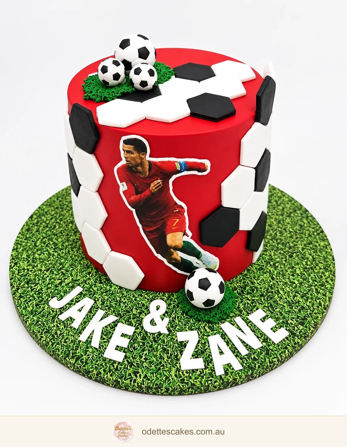 Red football birthday cake with a footballer decoration, black and white panels and footballs on a green pitch-style board, Jindalee, Perth