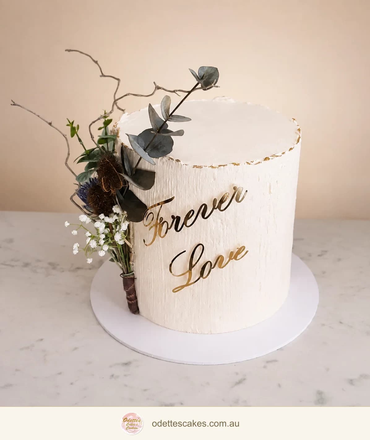 Single-tier ivory wedding cake with gold Forever Love lettering and a small dried floral arrangement