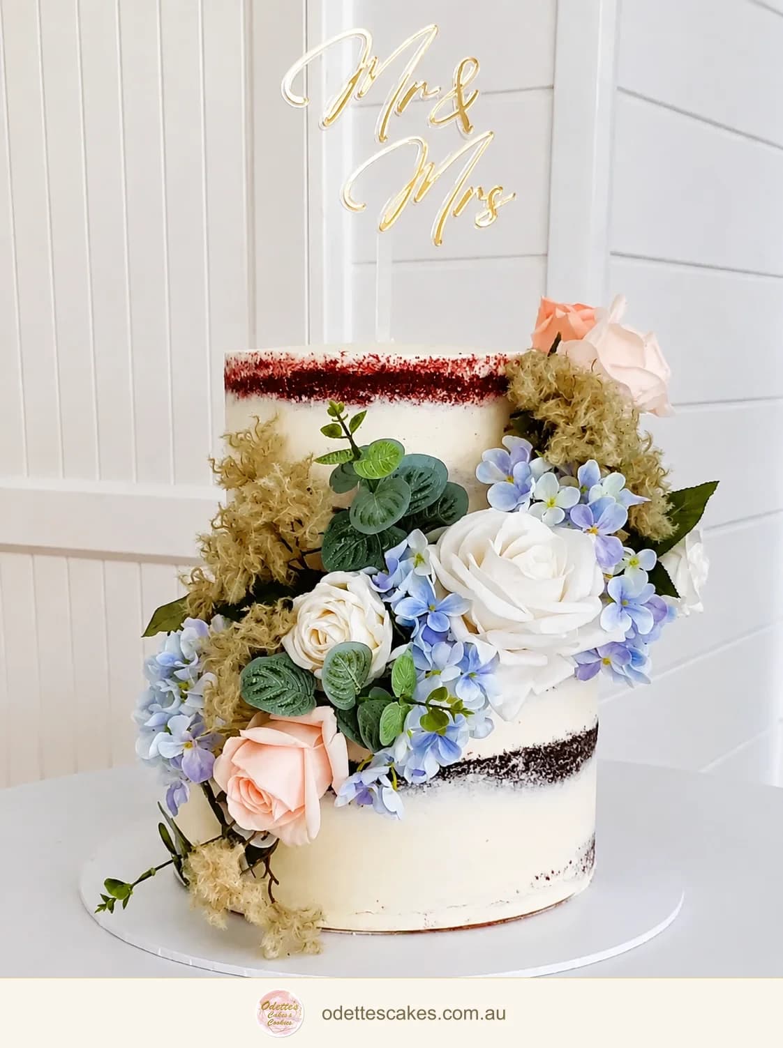 Three-tier semi-naked wedding cake with abundant pastel flowers and a gold Mr and Mrs topper