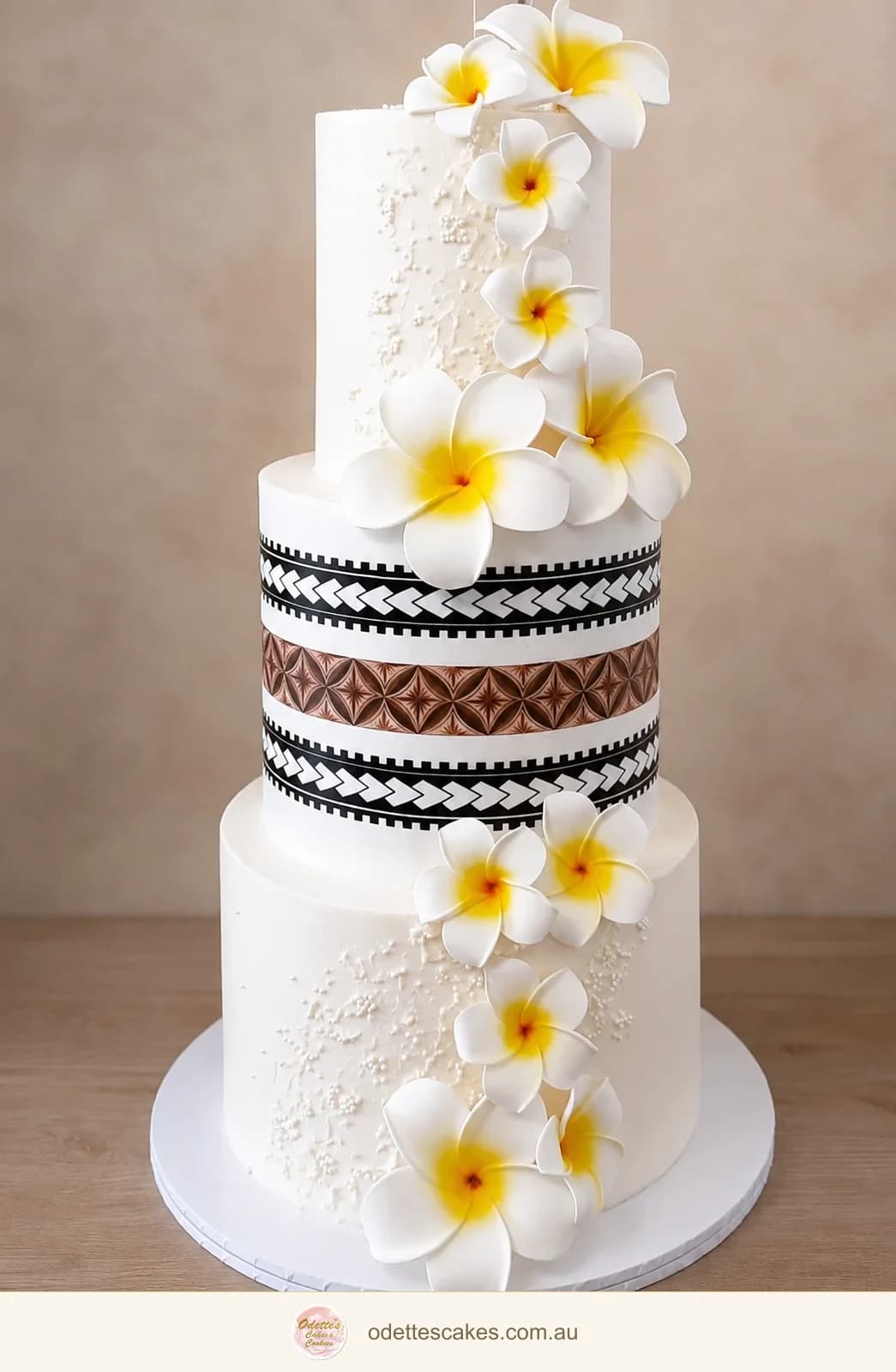 Tall white wedding cake with yellow-centred frangipani flowers and patterned black and brown bands