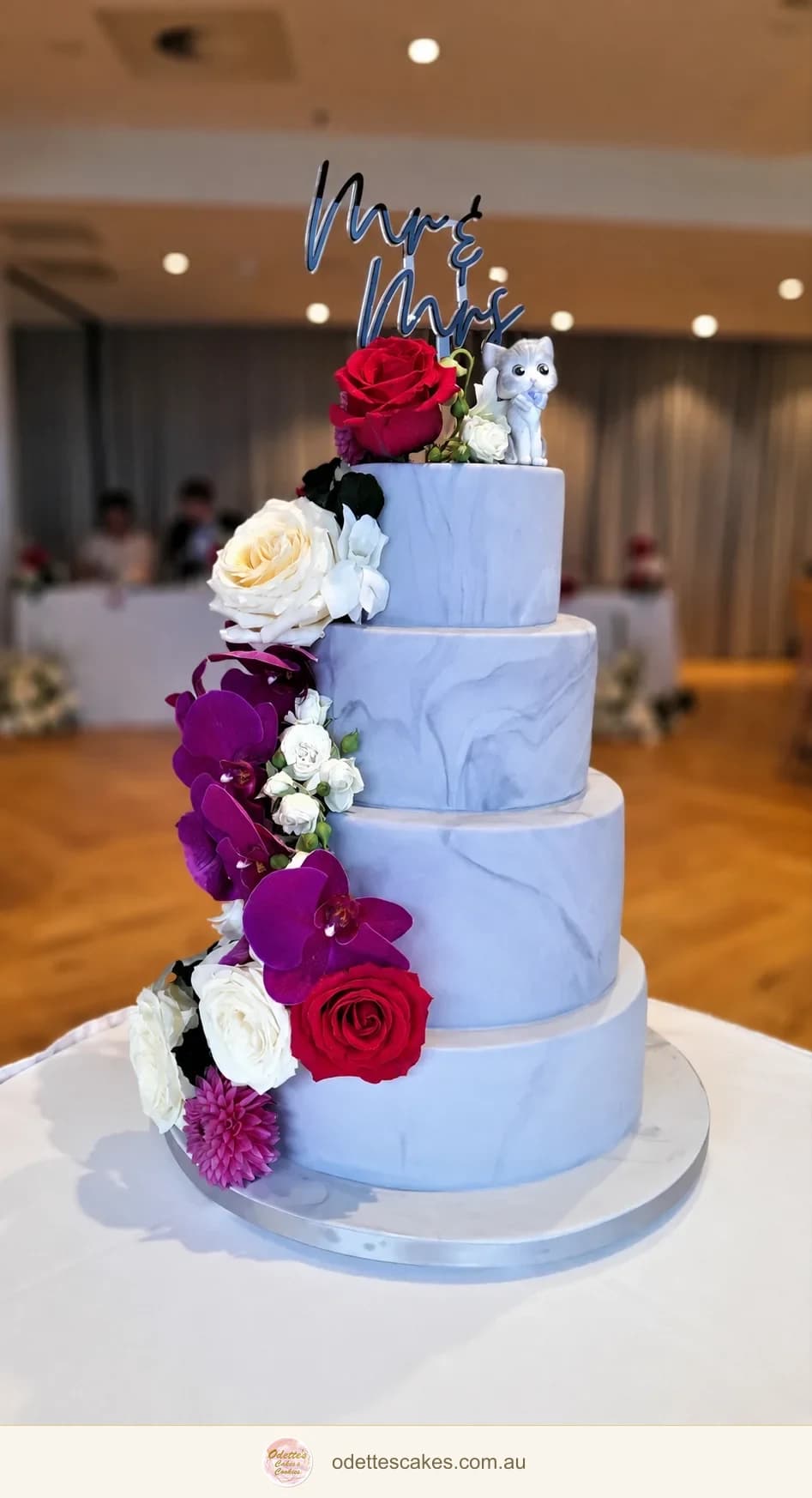 Three-tier pale lavender wedding cake with a cascade of purple, red and white flowers