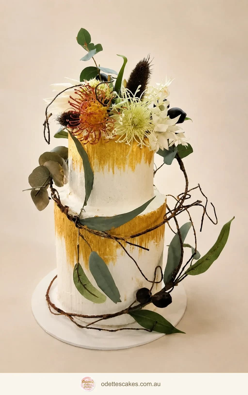 Two-tier cream wedding cake with Australian native flowers, eucalyptus and trailing branches
