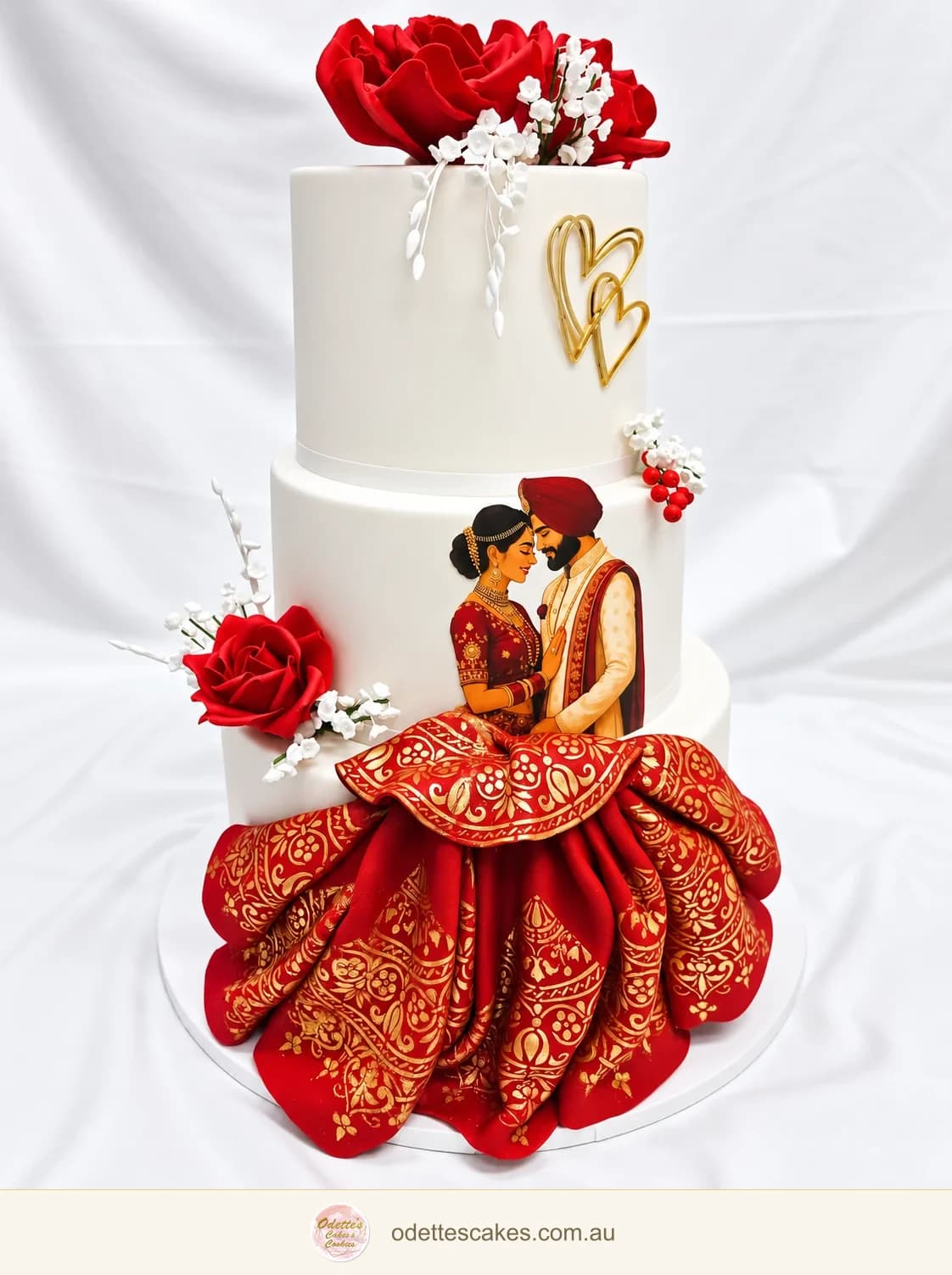 White tiered wedding cake with red roses, gold hearts and an illustrated couple above a sculpted red and gold skirt, made in Jindalee, Perth