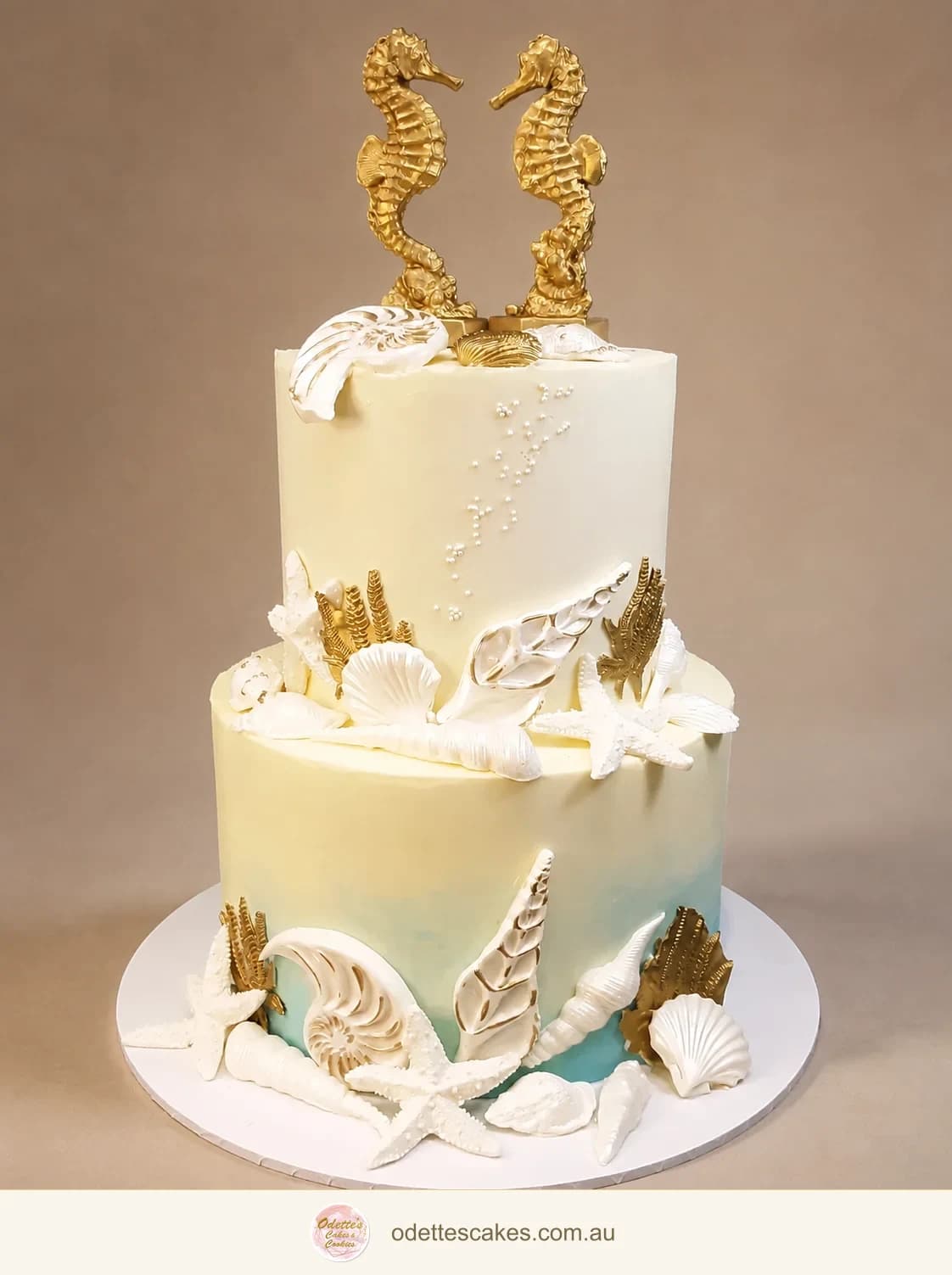 Two-tier ivory wedding cake with sculpted shells, coral details and two gold seahorse toppers