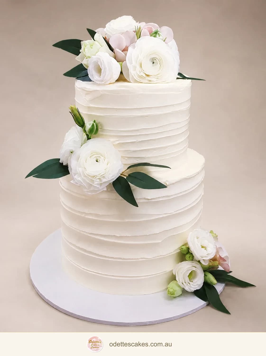 Two-tier white wedding cake with rippled buttercream, white flowers and dark green leaves