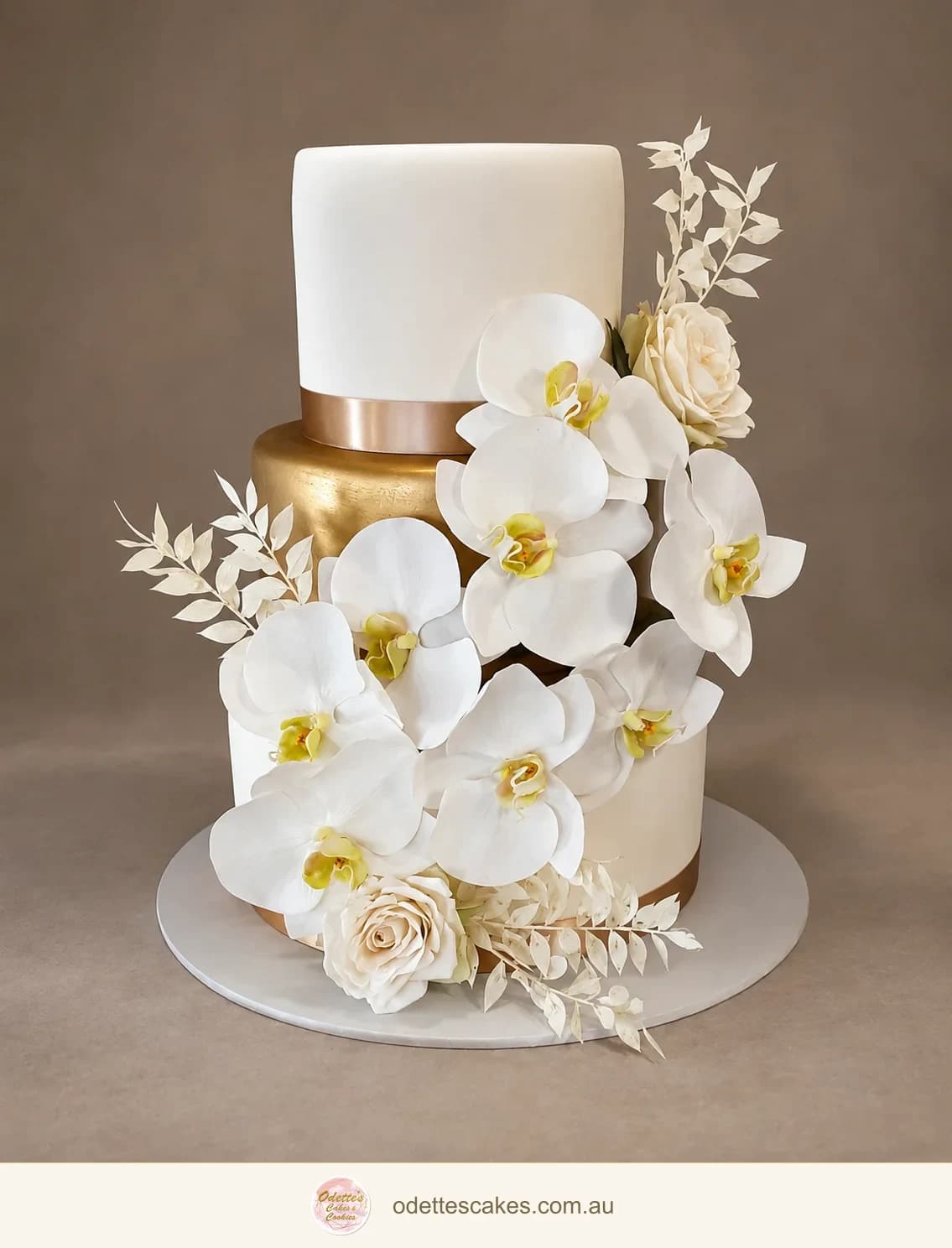Three-tier ivory wedding cake with cascading white orchids and gold ribbon details