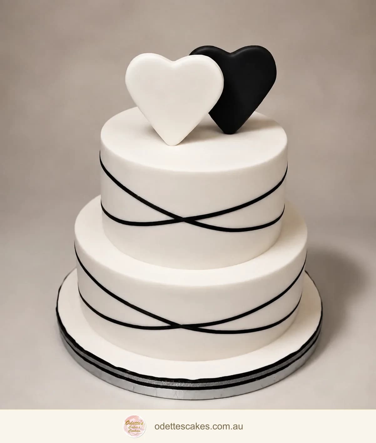 Two-tier white wedding cake with fine black ribbon lines and white and black heart toppers
