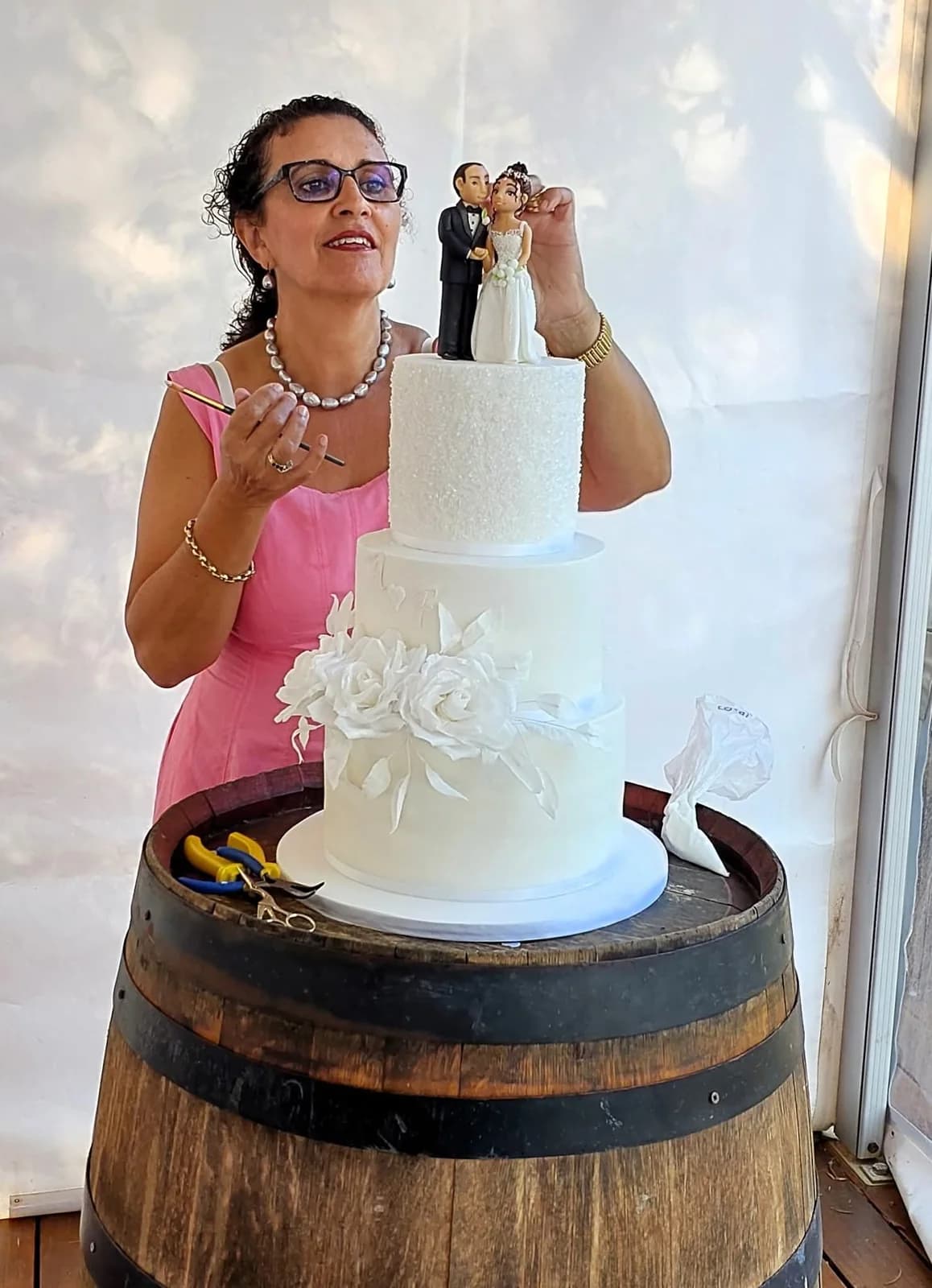 Odette carefully placing a couple figurine on a white three-tier wedding cake